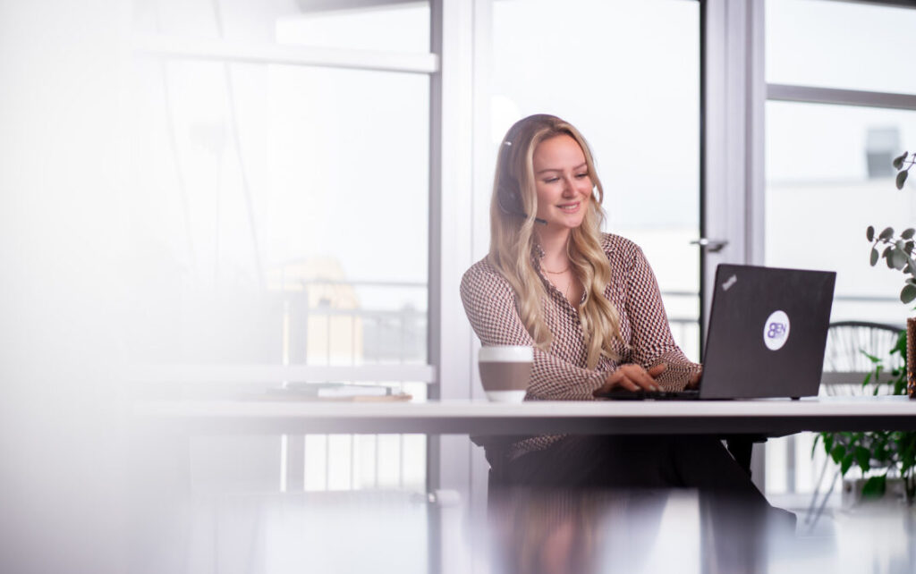 Dame sitzt freundlich mit dem Headset vor dem Laptop