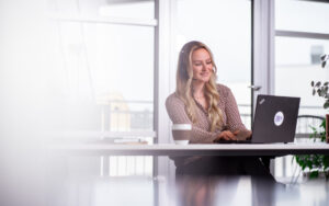 Dame sitzt freundlich mit dem Headset vor dem Laptop