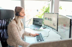 Frau die mit Headset vor dem Bildschirm sitzt