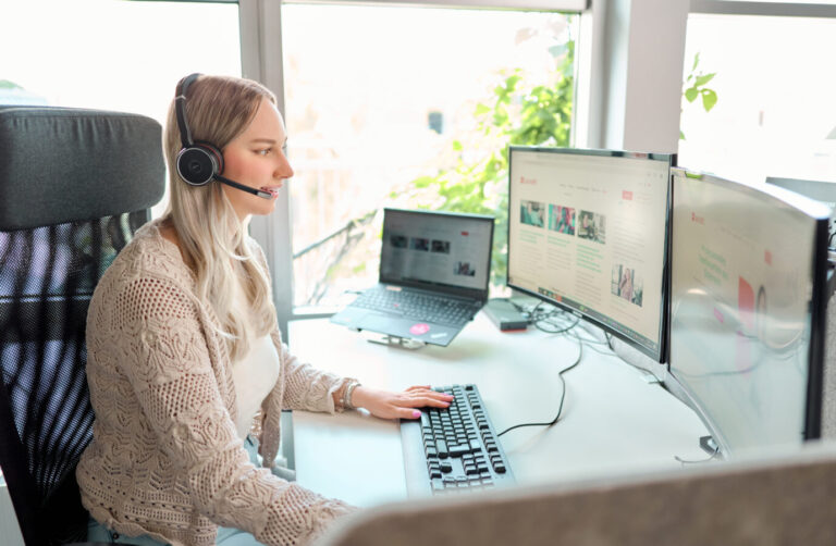 Frau die mit Headset vor dem Bildschirm sitzt